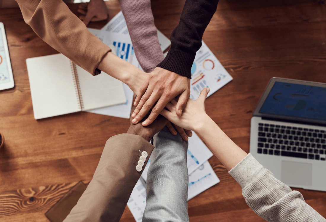 Managers in a meeting putting their hands together to showcase teamship after having resolved a conflict.